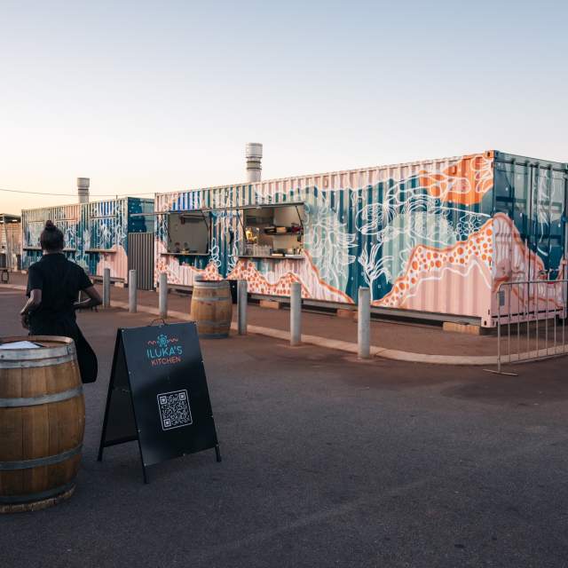 Shipping containers decorated with art representing the sea, which house pop-up food vendors at Marapikurrinya Park, Port Hedland.