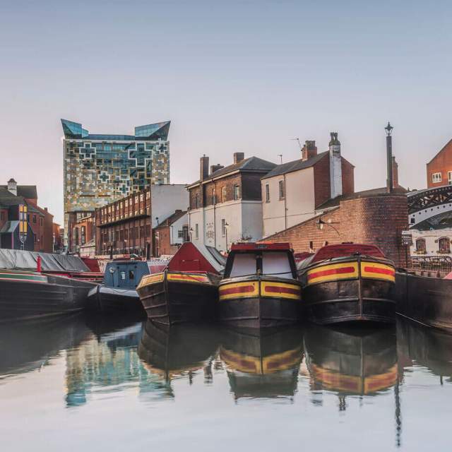 Canal boats moored at Gas Street Basin Birmingham in front of bring building a a large cubed glass building behind