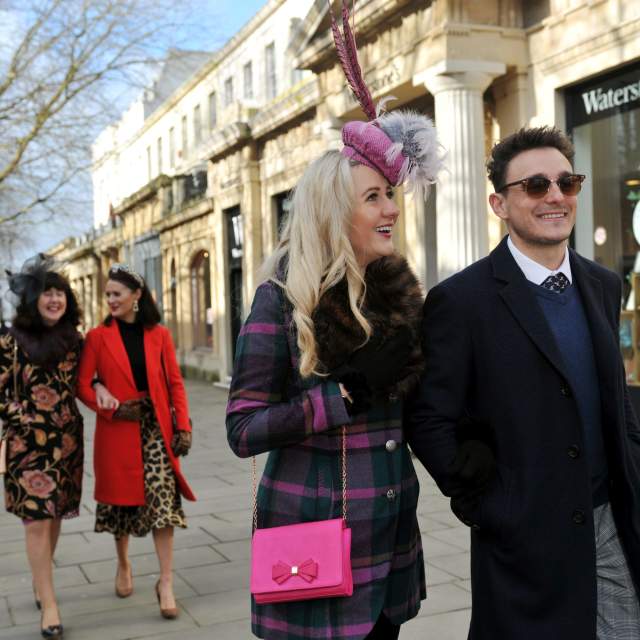 Friends dressed in racewear walking down The Promenade in Cheltenham.