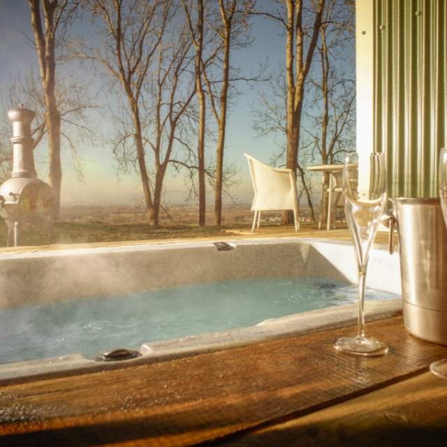 Hot tub bath at the Hilly Huts on FArncombe Estate. Steam rising from tub with bottle of sparkling wine, glasses and chimnea in background