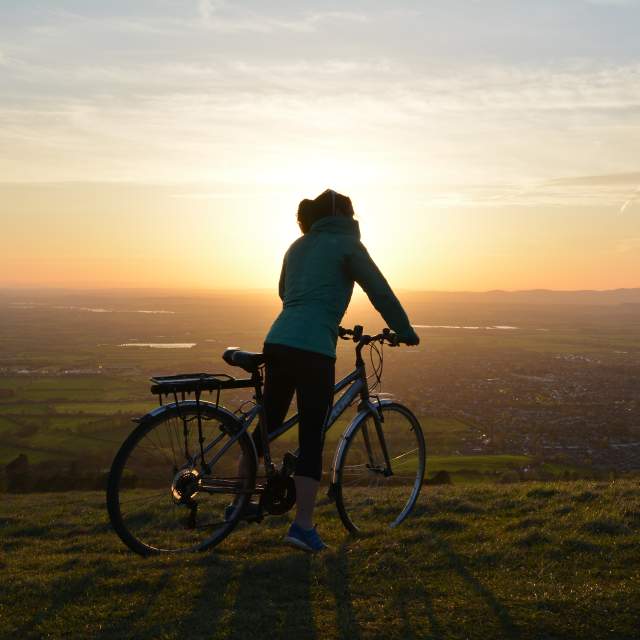 A cyclist enjoying the view of the setting sun near Cleeve Hill