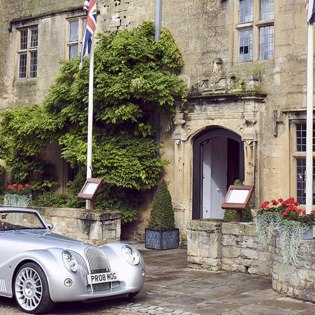 A vintage car parked in front of the Cotswold stone entrance to The Lygon Arms in the Cotswolds
