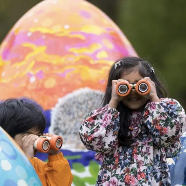 children in puddlesuits looking through binoculars, huge easter eggs in the background