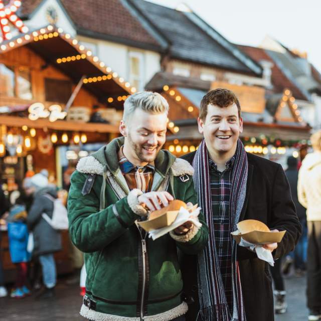 2 people eating street food. Festive lit buildings in the background