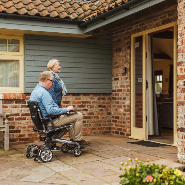 Man in motorised wheelchair with lady entering a cottage with level access