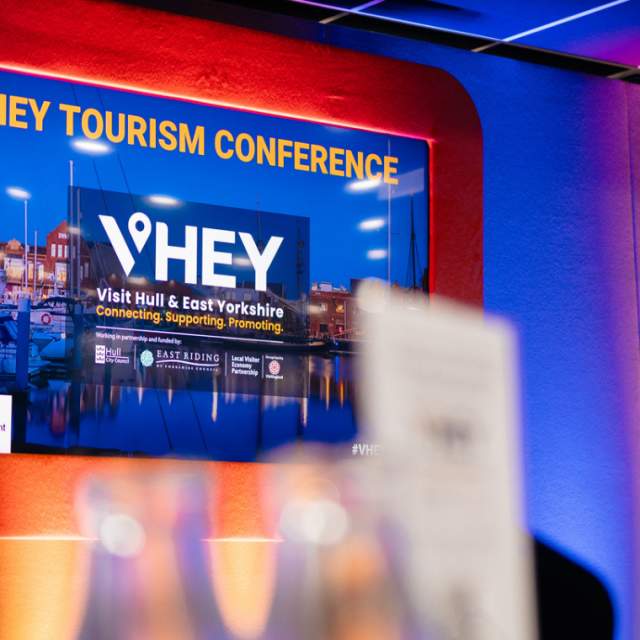 A screen on stage at the VHEY tourism conference 2024 displaying the VHEY logo.