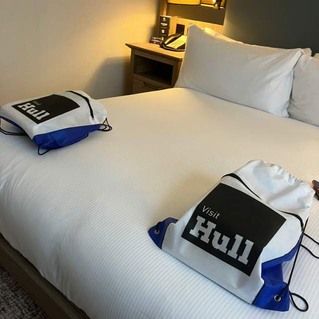 Large Bed in Hotel room with 2 Visit Hull drawstring bags