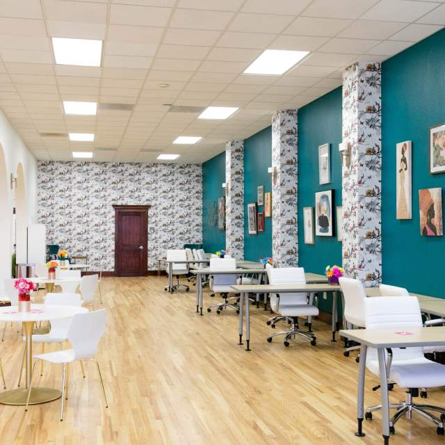 An artfully tasteful space with a turquoise accent wall with small desk spaces and several small tables.
