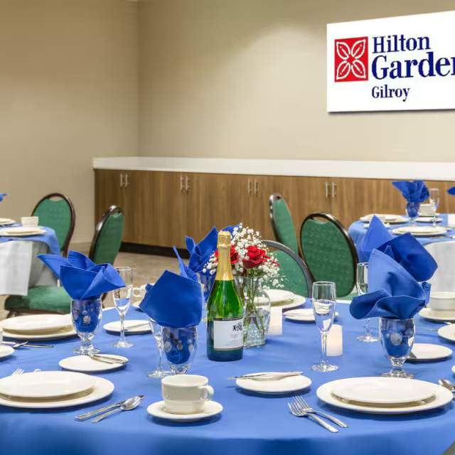 Hilton garden Inn Gilroy Banquet Room shows round dinner tables set with dinnerware