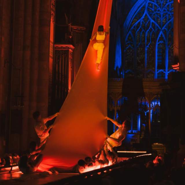 An event during Freedom Festival in Hull Minster with a dancer climbing up a long sheet held by 2 other performers