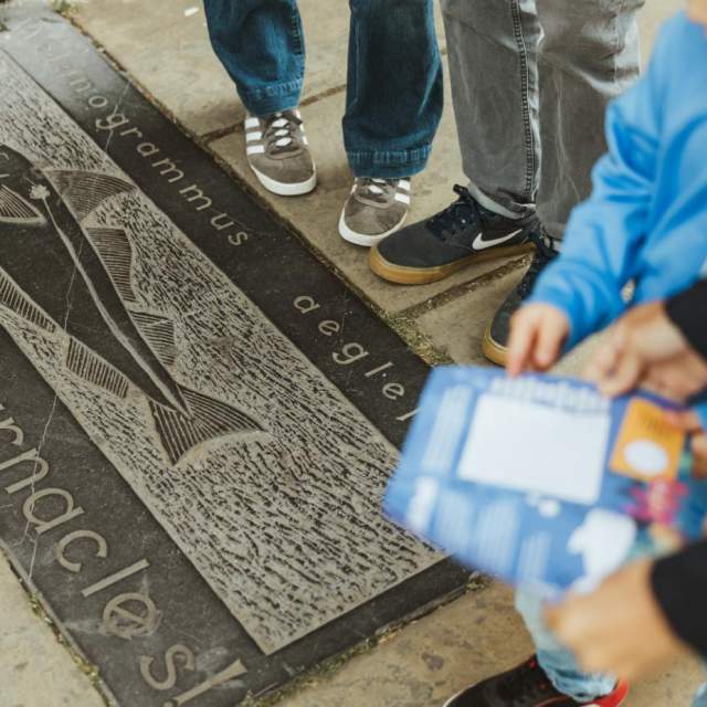 Stone plaque on Hull’s Fish Trail featuring an engraved fish illustration and species name, with visitors standing nearby while following the trail.