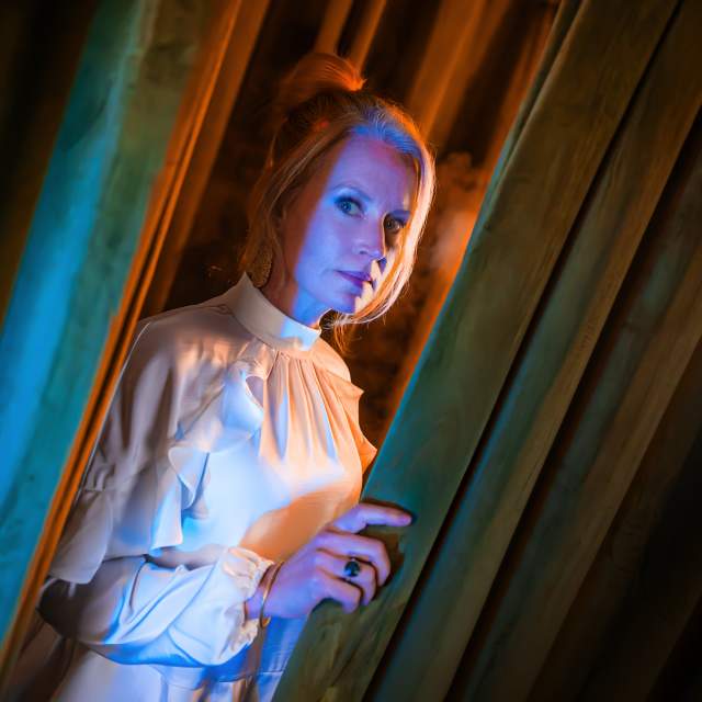 A still from the play Isabelle by Marc Graham. A woman in a white dress peers out from behind a partially opened door.