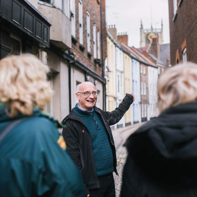 Group walking tour exploring Hull’s historic Old Town, with a guide pointing towards colourful period buildings along a narrow cobbled street.