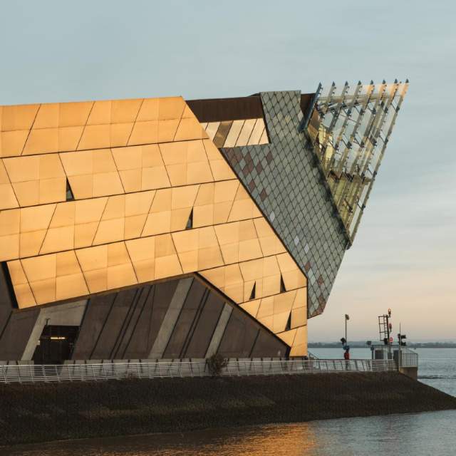 Exterior view of The Deep aquarium in Hull, showing the iconic angular building with golden panels overlooking the Humber estuary at sunset.