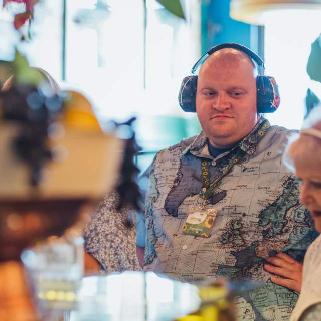 A customer wearing noise‑reducing headphones receives support while visiting an accessible café, highlighting sensory‑friendly environments and inclusive dining options