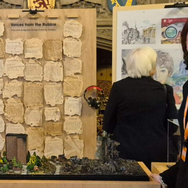 Yeseniia Serdiuk stands next to her art exhibition in a black top and lanyard