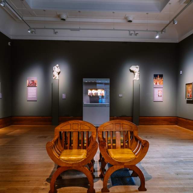 2 chairs facing the camera in the Ferens art gallery with paintings hung on the dark blue walls around.