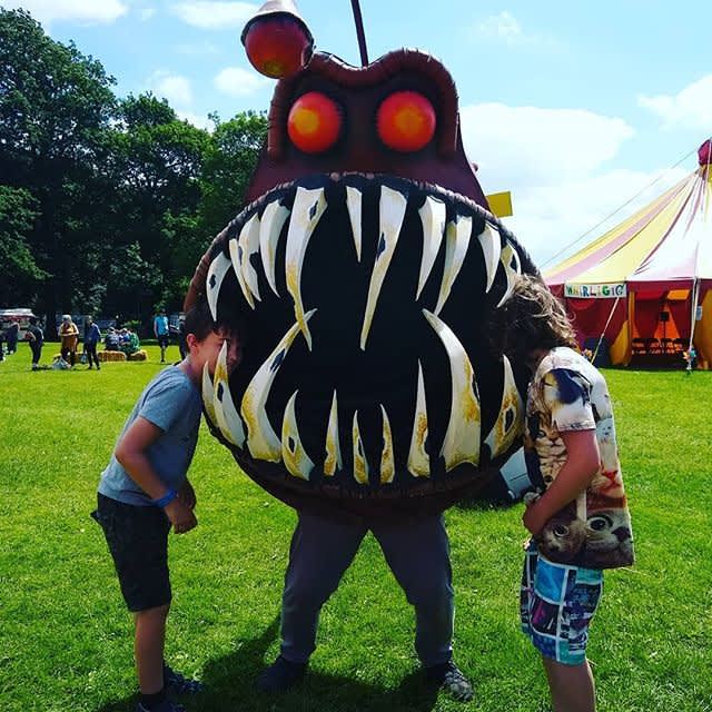 A giant fish character with sharp teeth stood with 2 children.