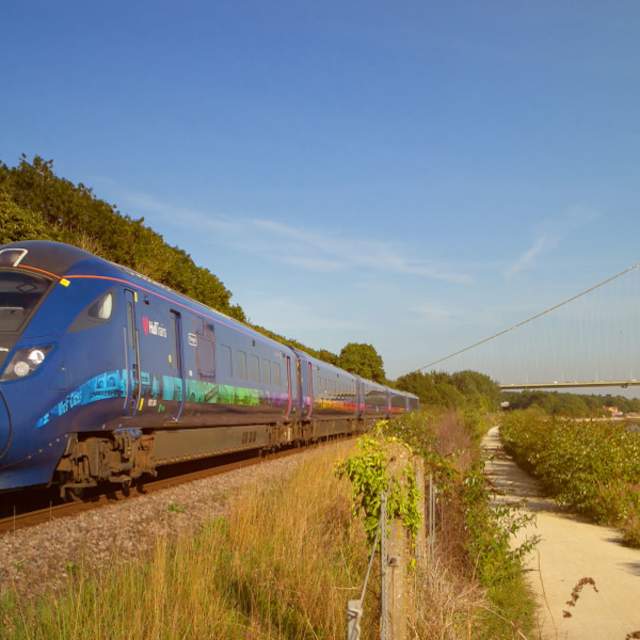 Blue Hull Trains trains speeding past the Humber Bridge (towards the camera) on a sunny day.