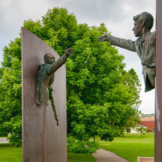 two statues of Martin Luther King Jr and Robert Kennedy reaching for one another. Trees and blue skies in background