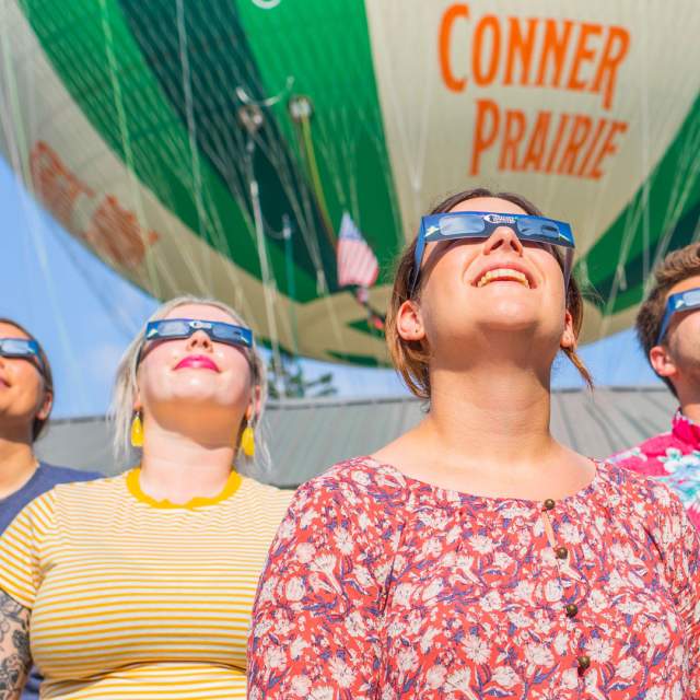 A group of four people stand looking at the sky with eclipse glasses on.