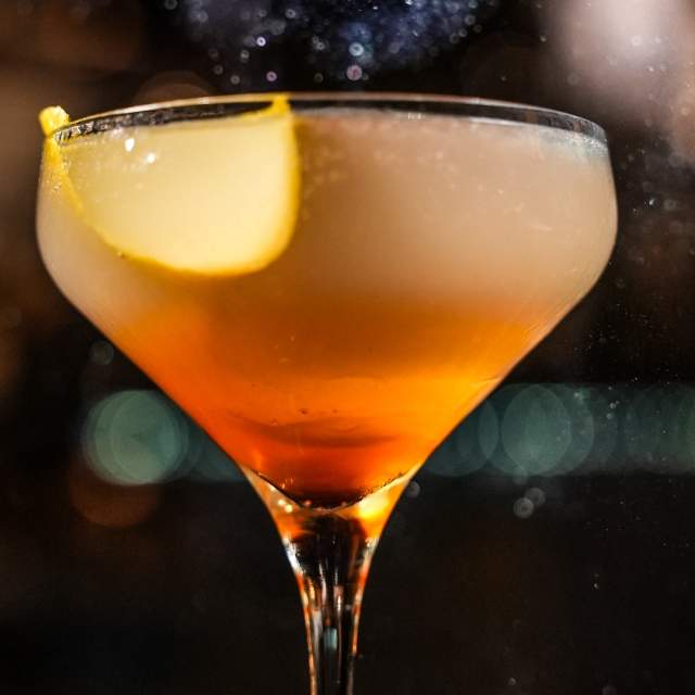 A cocktail coupe glass with sparkling liquid and a lemon garnish