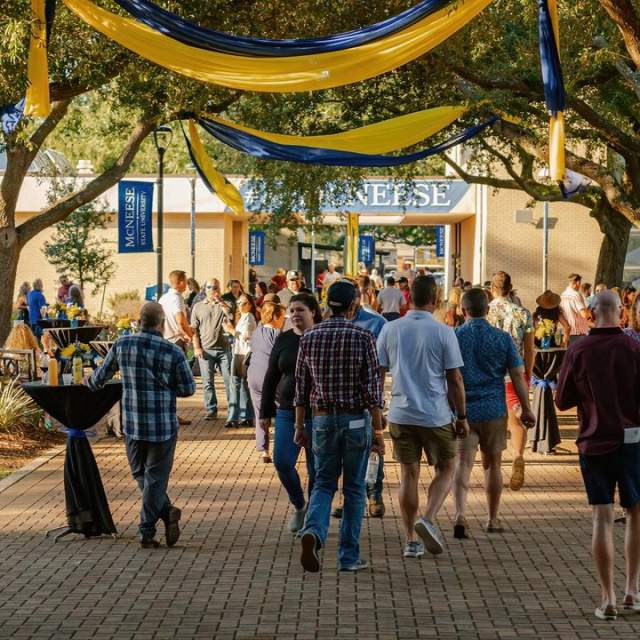 group of people walking in McNeese quad with blue and yellow decorations hanging from the oak trees
