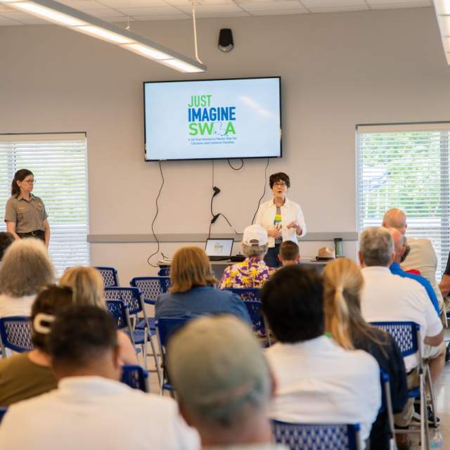 group of people listen to a presentation about Just Imagine SWLA