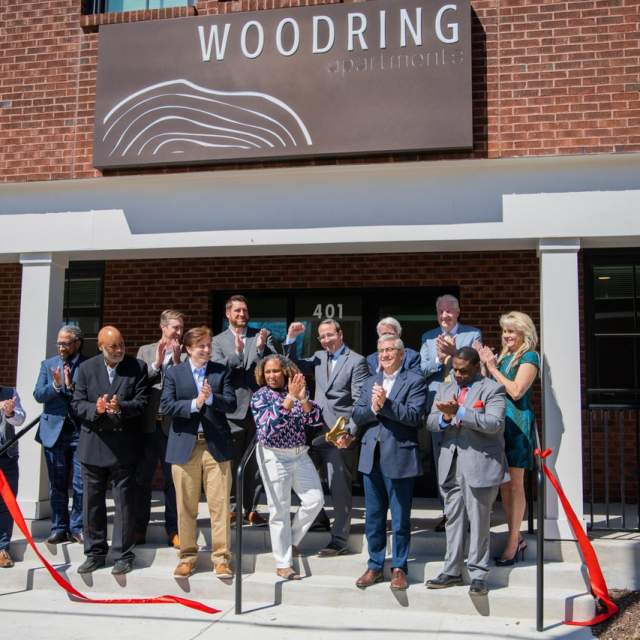 group of people at ribbon cutting on the steps of woodring apartment complex