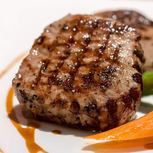 A perfectly cooked juicy steak served on a white plate, accompanied by vibrant steamed carrots, fresh broccoli florets, and tender asparagus spears.
