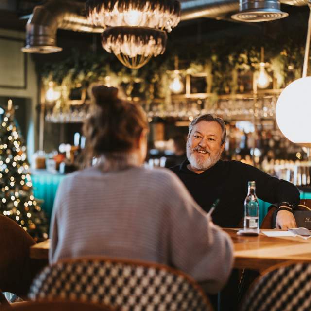 A man smiling at an interviewer sat on a table in a bar in Away Resorts
