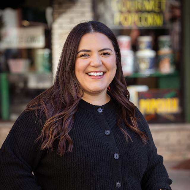 A woman with dark hair and a black cardigan standing in front of a popcorn shop.