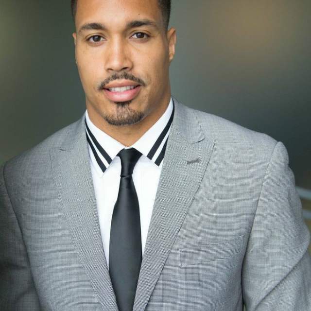 Headshot image of Travis Beckum, a Black man wearing a suit.