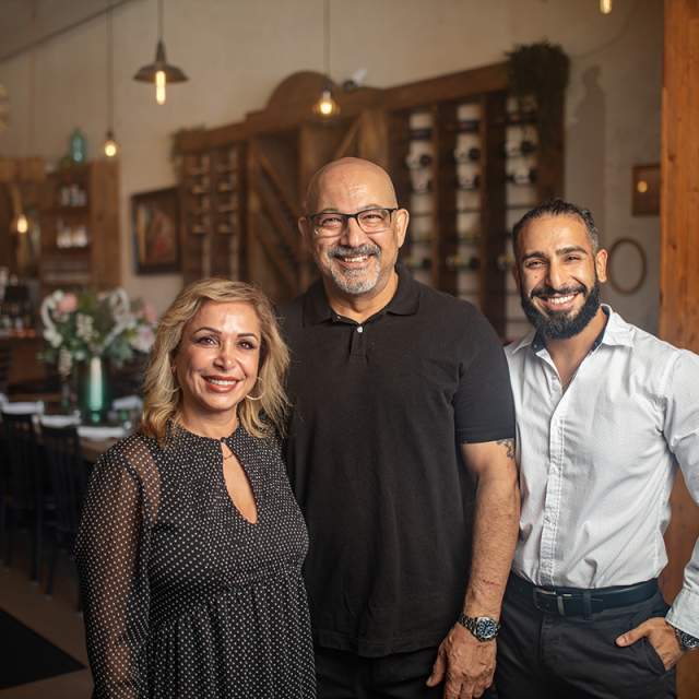 One woman and two men smiling and standing in front of a table in a restaurant