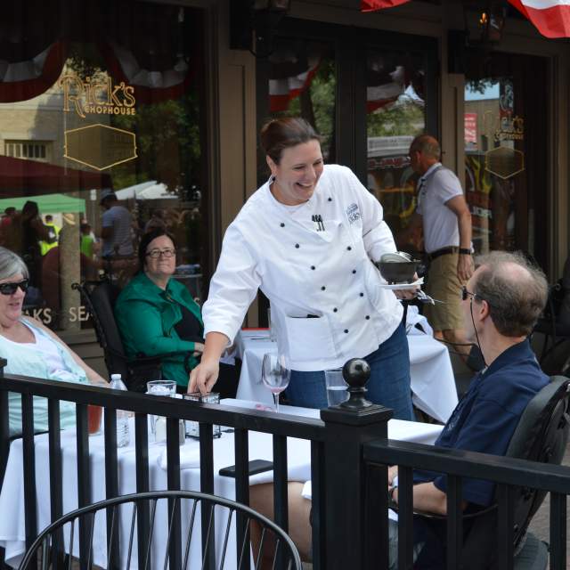 Young woman serving an older couple at a table on a patio at Rick's Chophouse
