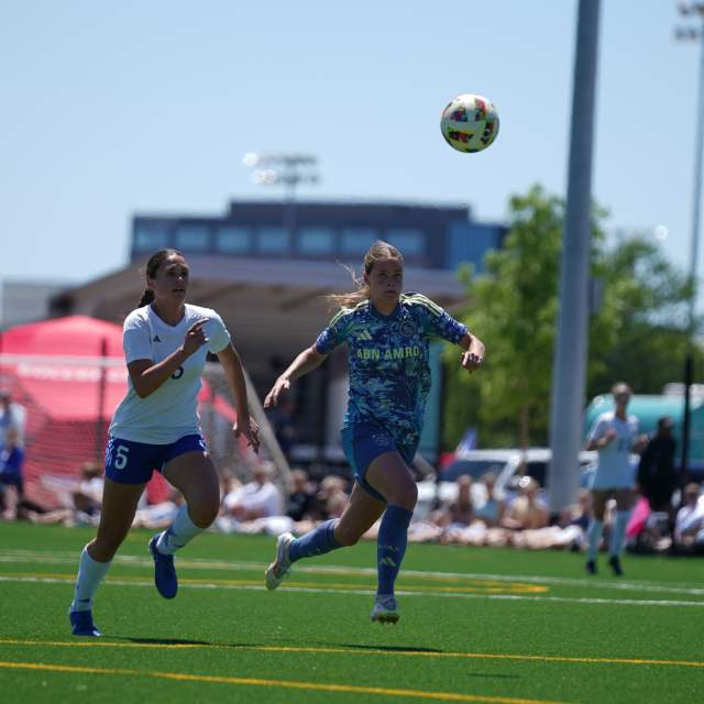 Two people running after a soccer ball on a turf field