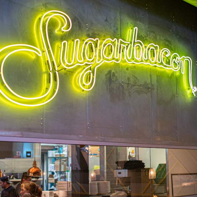Yellow script neon Sugarbacon sign over kitchen opening