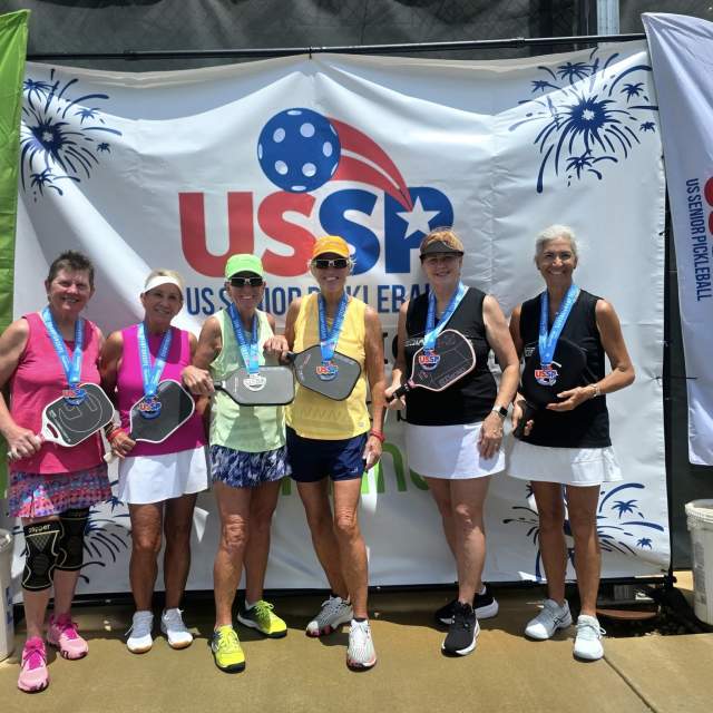 Group of people posing with pickleball paddles and medals around their necks at the US Senior Pickleball tournament