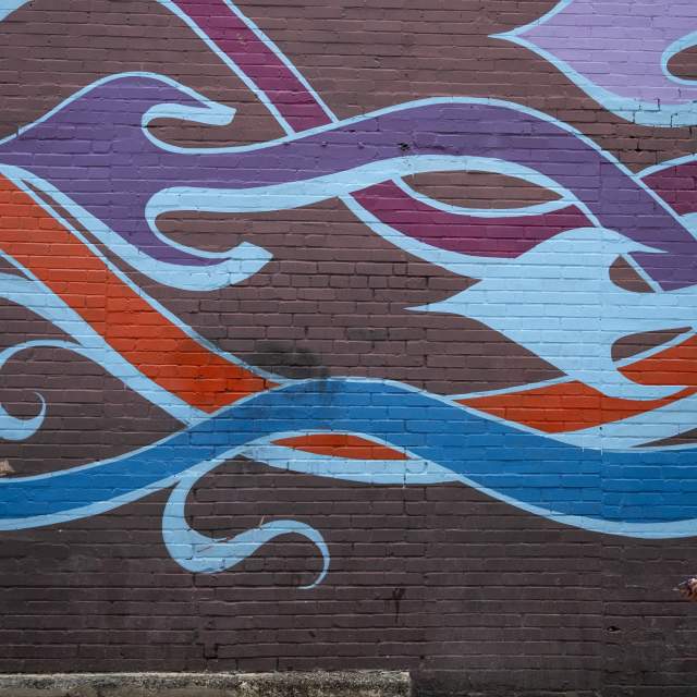 Graffiti art on a brick wall with arrows snaking across it. A young girl stands looking up at the mural