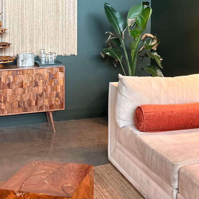 Off-white couch with a burnt orange pillow and square ottoman in front of it