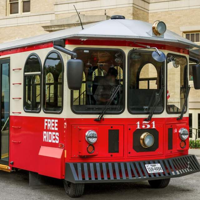 Downtown McKinney Trolley - red and beige - on front of large cream colored building