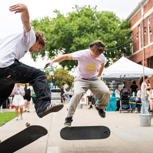Two people kick flipping their skateboards in the air