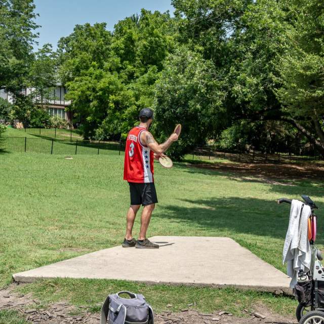 Two men playing disc golf. One man dressed in red is preparing to throw the frisbee