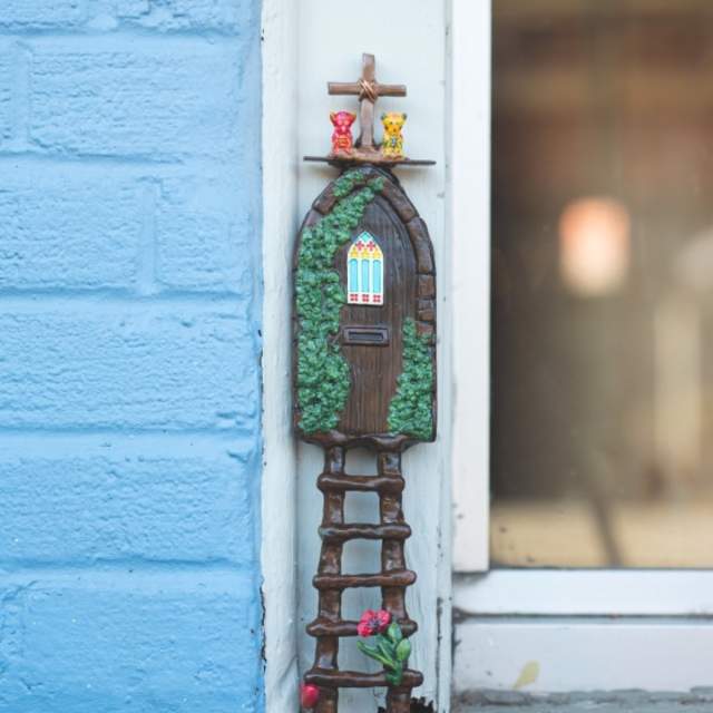Tiny fairy door that is nature themed with a ladder leading up to the door