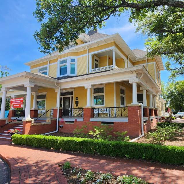 Big yellow house with hedge around red brick sidewalk leading to steps