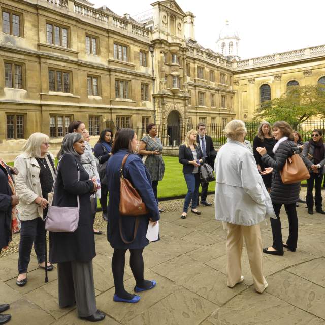 A group of people listening to a walking tour guide in the grounds of a Cambridge College