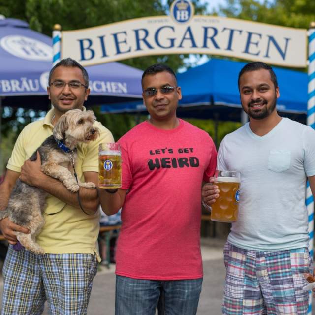 Three men and a dog at the Estabrook Beer Garden, smiling and holding steins of beer.