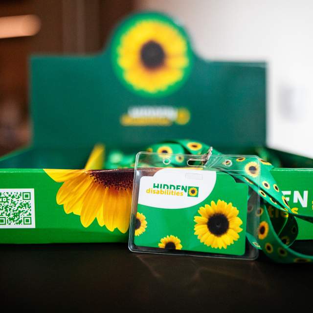 a "Hidden Disabilities" ID card and lanyard are displayed in front of a green sunflower-themed box.