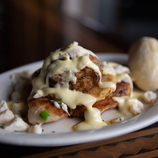 Blackened fish with cream sauce and lump crab meat and a roll on a white oval plate