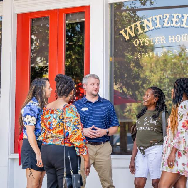 A male tour guide stands outside Wintzell's Oyster House with four female tourists